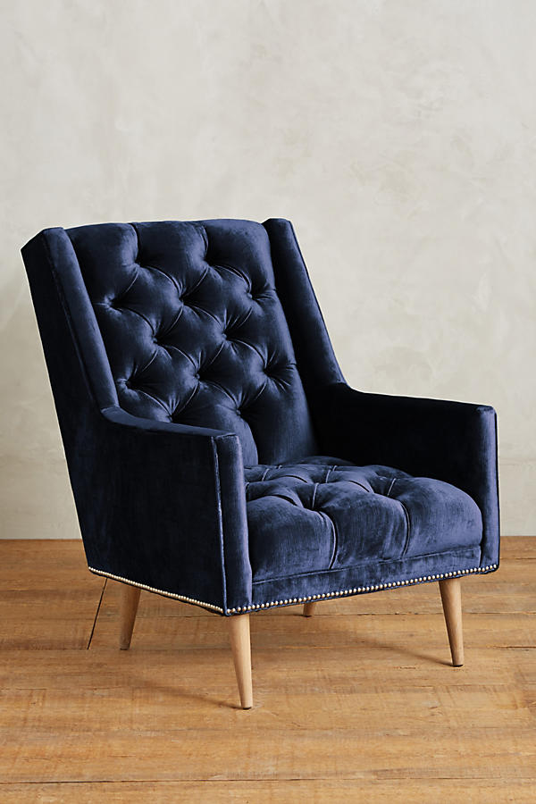 Sillón individual tapizado en azul, con respaldo capitoné de botones, brazos rectos y patas de madera inclinadas.