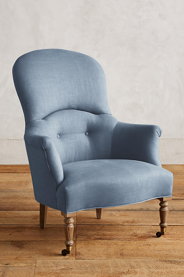 Sillón individual de diseño tradicional en tono ceelste, con respaldo curvo, apoyabrazos tallados y patas delanteras de madera con ruedas.