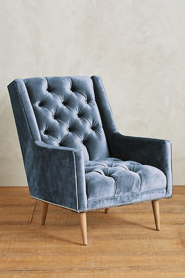 Sillón individual tapizado en celeste, con respaldo capitoné de botones, brazos rectos y patas de madera inclinadas.