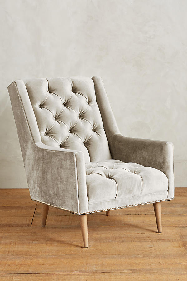 Sillón individual tapizado en crema, con respaldo capitoné de botones, brazos rectos y patas de madera inclinadas.