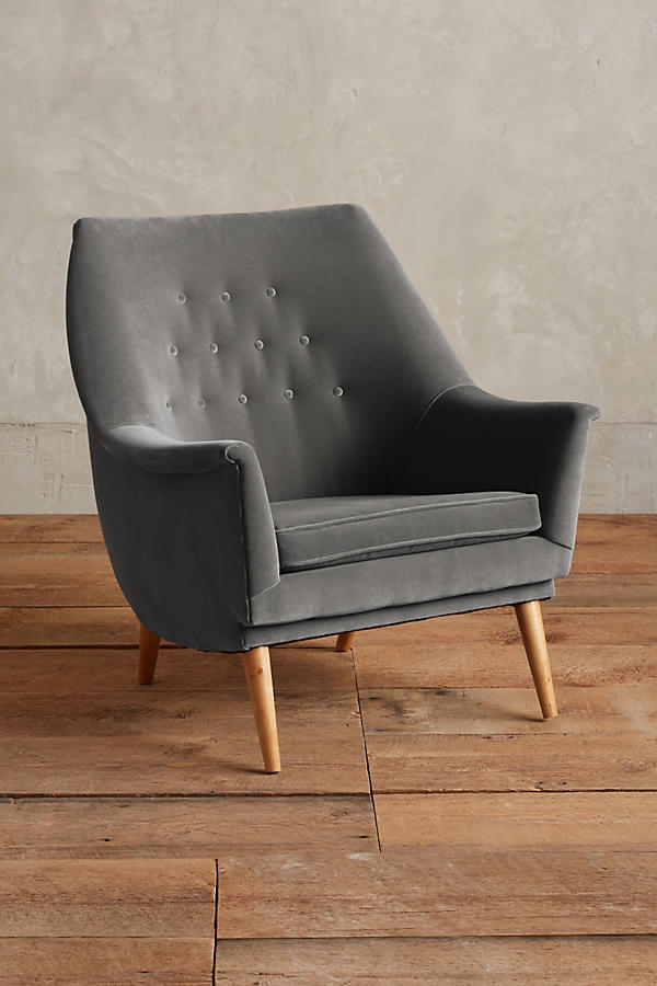 Sillón individual tapizado en terciopelo gris oscuro, de diseño retro con respaldo inclinado, asiento acolchado y patas de madera inclinadas estilo escandinavo.