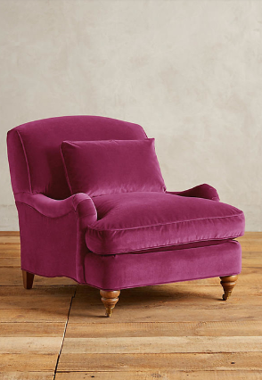 Sillón individual tapizado en magenta, con cojín lumbar suelto, apoyabrazos curvos, respaldo levemente inclinado y patas torneadas de madera en tono medio.