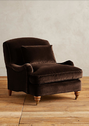 Sillón individual tapizado en marron, con cojín lumbar suelto, apoyabrazos curvos, respaldo levemente inclinado y patas torneadas de madera en tono medio.