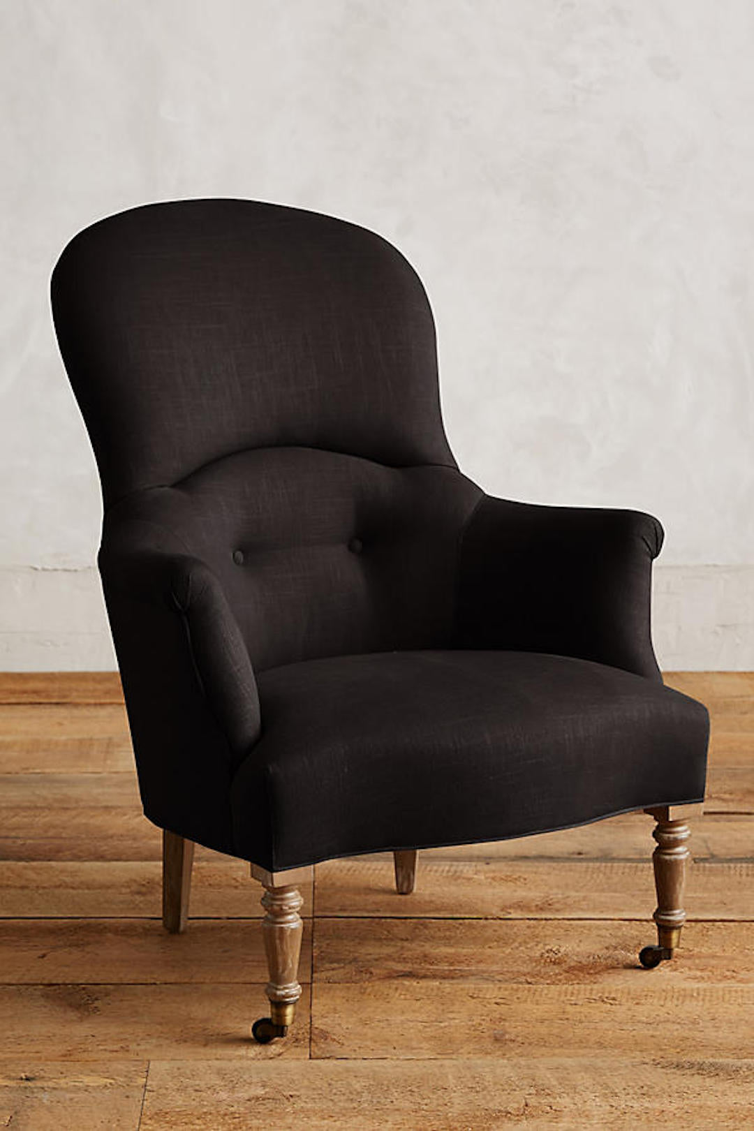 Sillón individual de diseño tradicional en tono negro, con respaldo curvo, apoyabrazos tallados y patas delanteras de madera con ruedas.