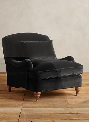 Sillón individual tapizado en negro, con cojín lumbar suelto, apoyabrazos curvos, respaldo levemente inclinado y patas torneadas de madera en tono medio.