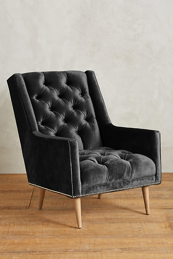 Sillón individual tapizado en negro, con respaldo capitoné de botones, brazos rectos y patas de madera inclinadas.