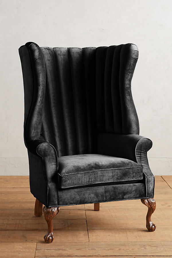 Sillón individual tapizado en negro, con respaldo alto acanalado de líneas verticales, brazos curvos y patas delanteras torneadas con ruedas pequeñas.