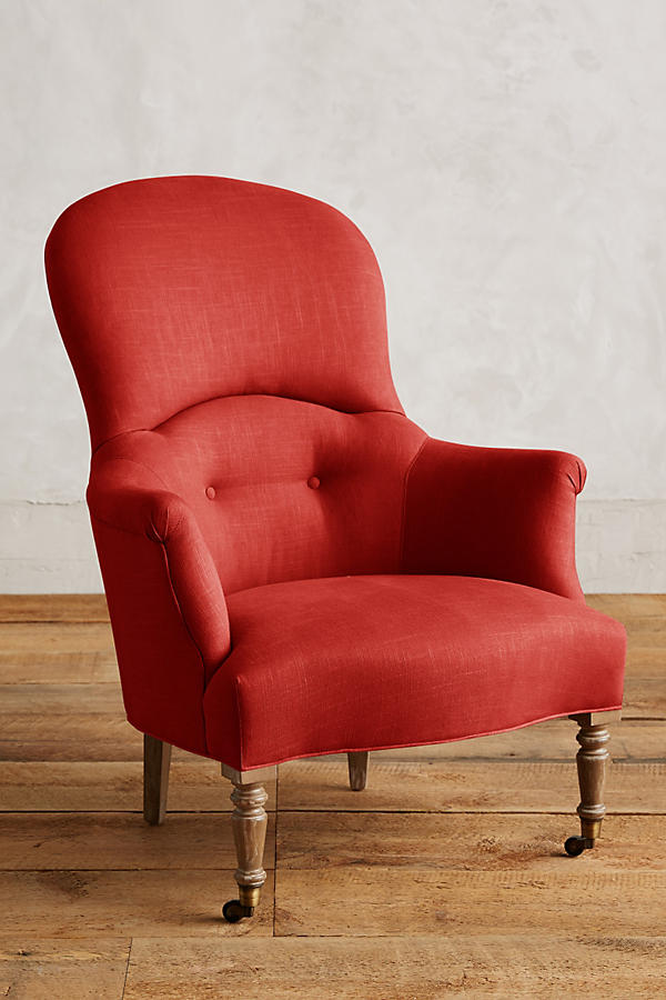 Sillón individual de diseño tradicional en tono rojo, con respaldo curvo, apoyabrazos tallados y patas delanteras de madera con ruedas.