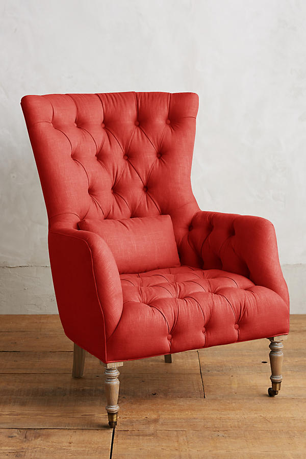 Sillón individual tapizado en rojo, con respaldo alto y capitoné, cojín lumbar suelto, brazos curvos y patas delanteras torneadas en madera clara.