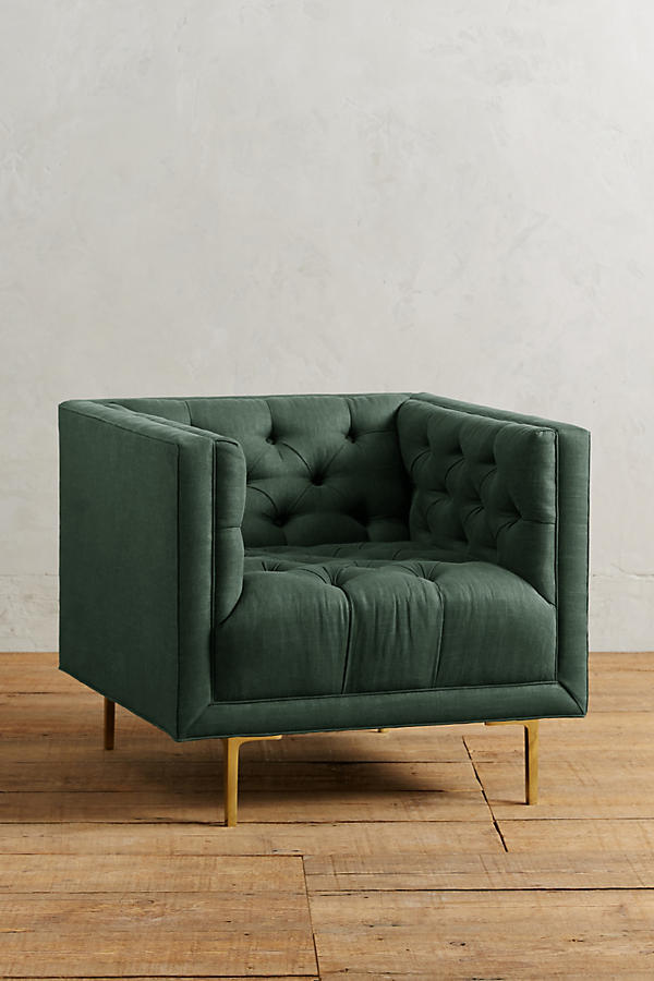 Sillón individual tapizado en verde, de forma cúbica con respaldo y brazos rectos, capitoné de botones en todo el interior y patas delgadas de madera.
