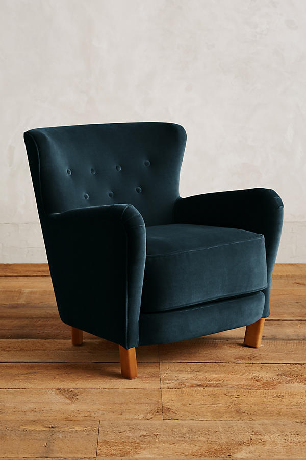 Sillón individual tapizado en verde azulado, con respaldo suavemente inclinado y capitoné de botones, brazos redondeados y patas cortas de madera.