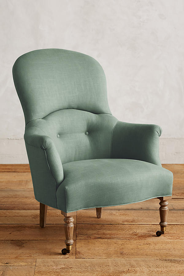 Sillón individual de diseño tradicional en tono verde claro, con respaldo curvo, apoyabrazos tallados y patas delanteras de madera con ruedas.