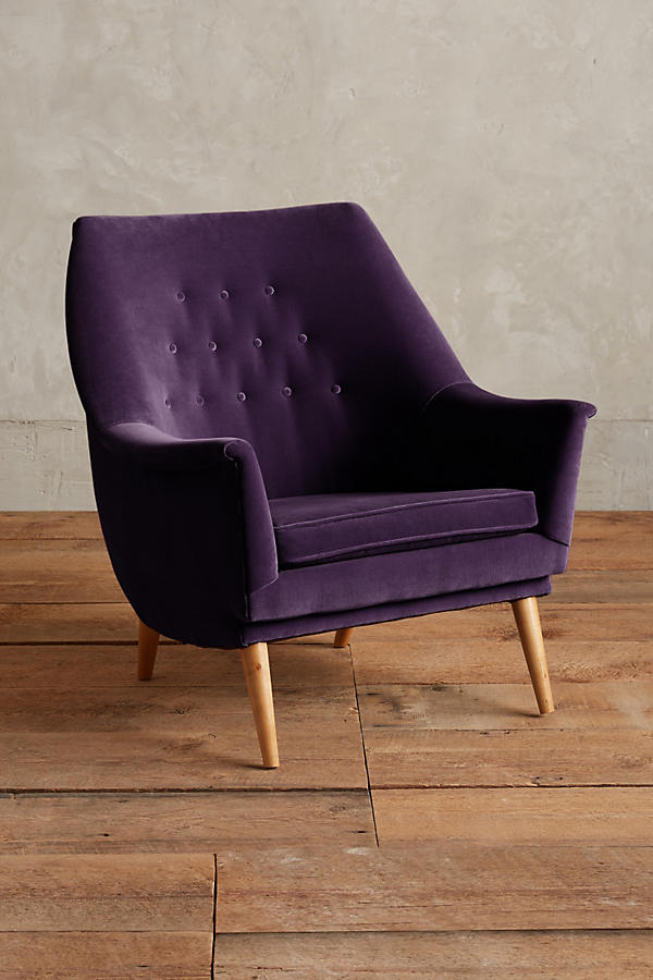 Sillón individual tapizado en violeta, de diseño retro con respaldo inclinado, asiento acolchado y patas de madera inclinadas estilo escandinavo.