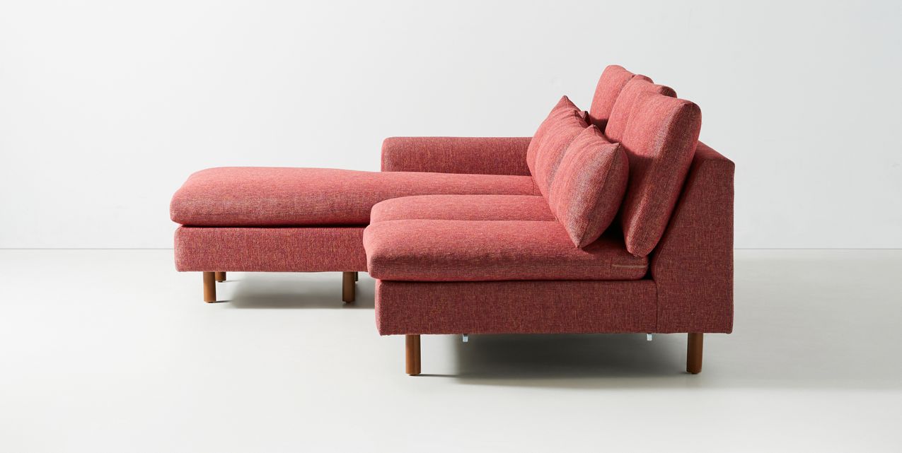 Sillón esquinero moderno en pana rosa oscuro, respaldo alto y estructura sólida con patas de madera natural.