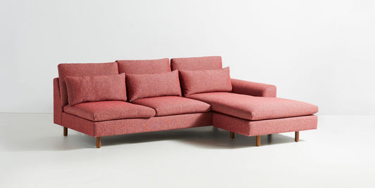 Sillón esquinero moderno en pana rosa oscuro, respaldo alto y estructura sólida con patas de madera natural.