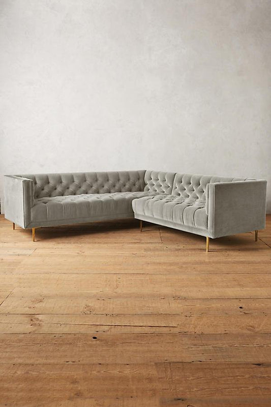 Sillón esquinero clásico en gris con respaldo capitoné profundo, apoyabrazos rectos y patas finas de madera. Diseño elegante y sofisticado.