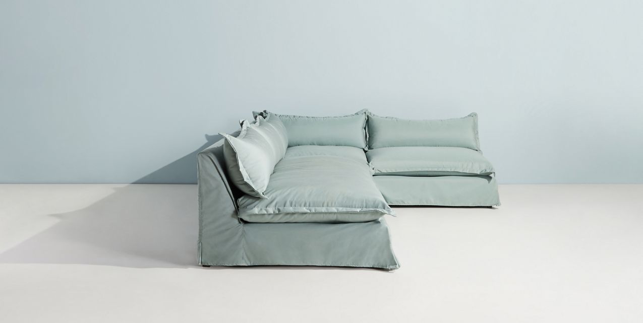Sillón esquinero grande en lino gris claro con respaldo bajo, almohadones sueltos y chaise longue. Diseño descontracturado y moderno.
