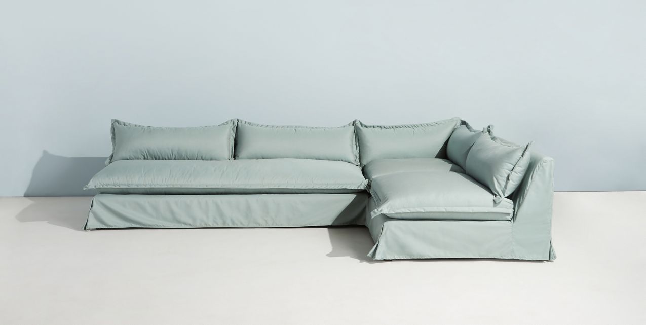 Sillón esquinero grande en lino gris claro con respaldo bajo, almohadones sueltos y chaise longue. Diseño descontracturado y moderno.