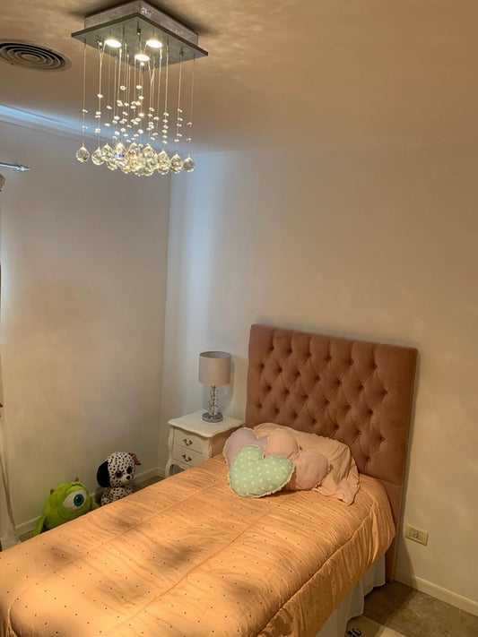 Dormitorio infantil con respaldo tapizado en terracota con capitoné en diamante, almohadones en forma de corazón y lámpara araña de cristales