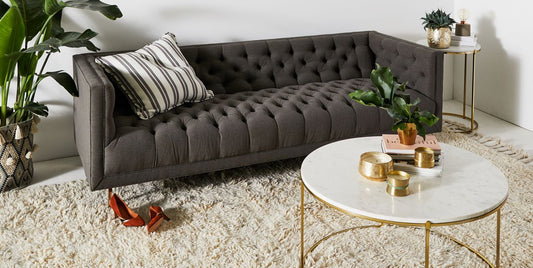 Sofá Bella Donna Capitoné tapizado en gris, ambientado en living con planta y mesa ratona - Tienda de Banquitos