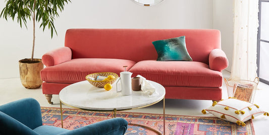 Sofá Cecily tapizado en velvet coral, ambientado en living luminoso con planta y mesa ratona - Tienda de Banquitos