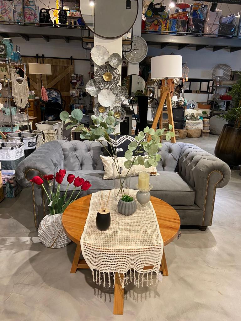 Vista general del Sofá Chesterfield gris con mesa de madera y flores en Hogar & Garden, Córdoba