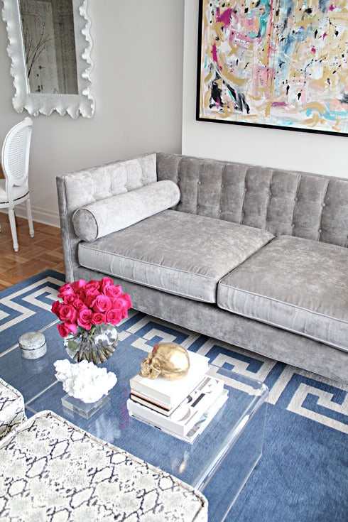 Sofá Valentino tapizado en velvet gris, con capitoné en el respaldo y almohadones cilíndricos, ambientado en living - Tienda de Banquitos