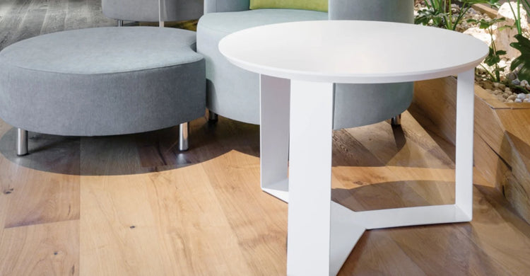 Mesa de arrime Janod de Archivos Activos blanca junto a sillones grises en un lounge