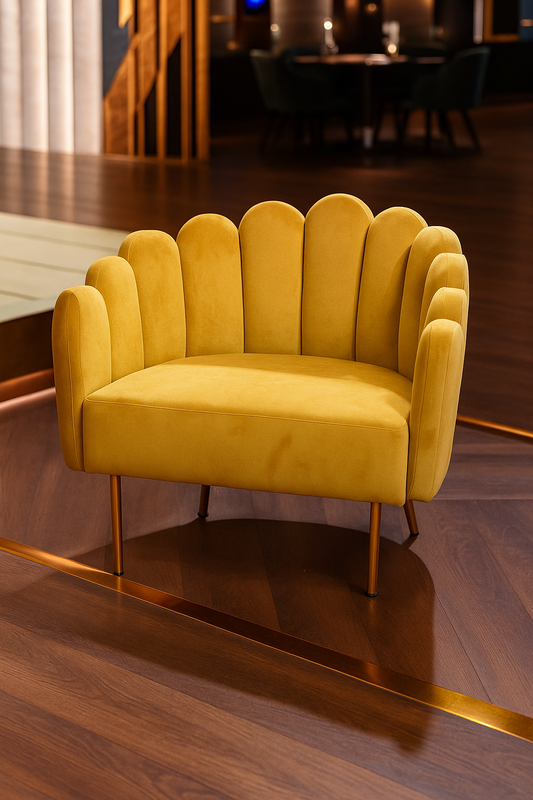 Sillón individual de diseño moderno con respaldo y brazos en forma de concha o pétalos, tapizado en terciopelo amarillo mostaza. Las patas delgadas de metal en acabado dorado complementan su estilo elegante y contemporáneo