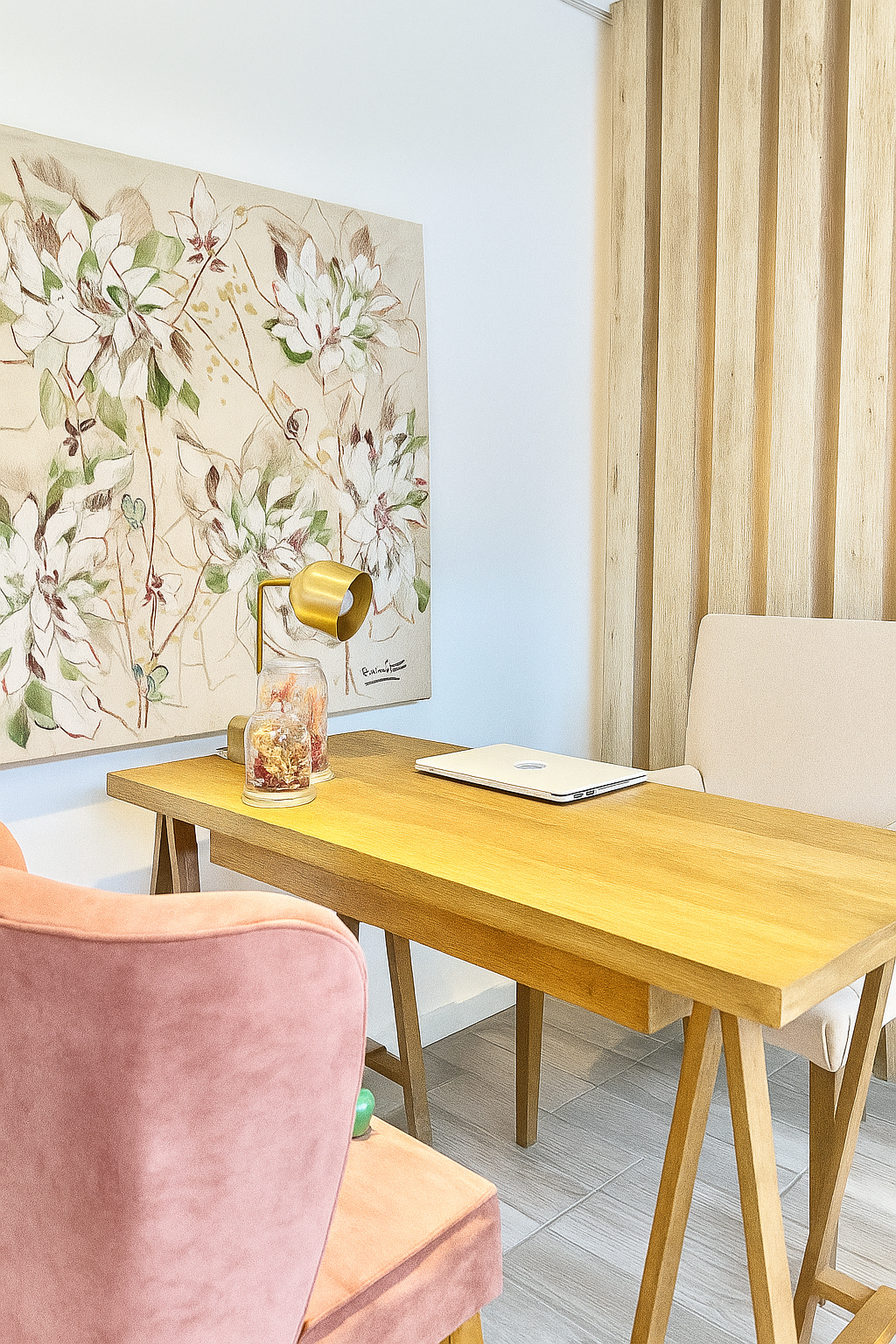 Escritorio de madera con silla beige y silla rosa, decorado con un cuadro floral en tonos claros colgado en la pared.