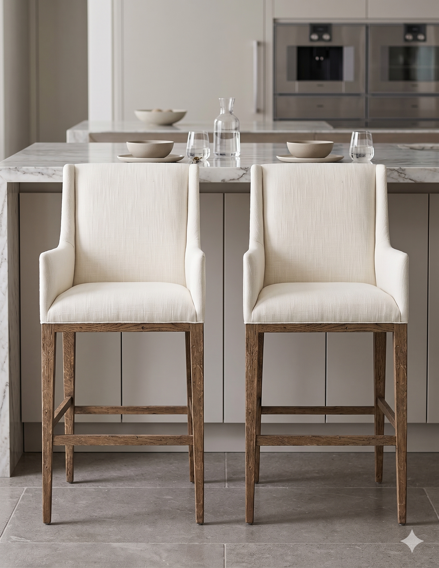 Banqueta alta de diseño contemporáneo con estructura de madera maciza en acabado natural. Presenta un asiento y respaldo integrado, tapizado en pana color claro con textura sutil. Incluye apoyapiés perimetral de madera para mayor estabilidad y confort