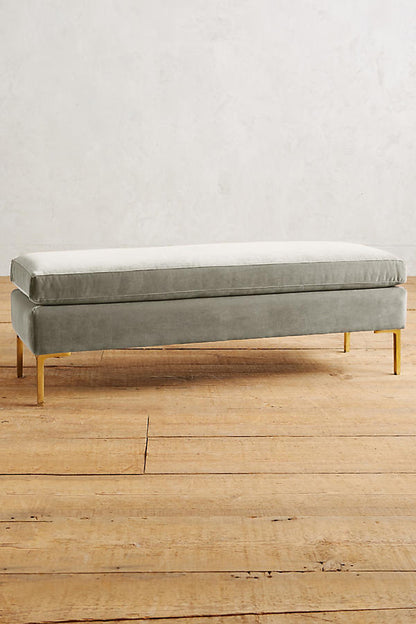 Banqueta de diseño moderno tapizada en  crema con patas metálicas doradas. Ideal para pie de cama, recibidores o livings.