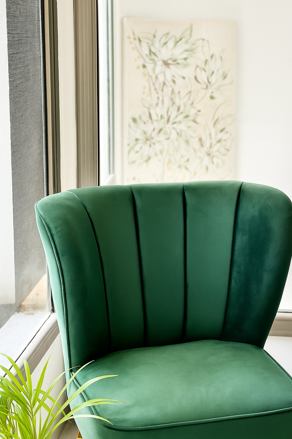 Sillón verde junto a una ventana, con un cuadro floral detrás de un vidrio en el fondo