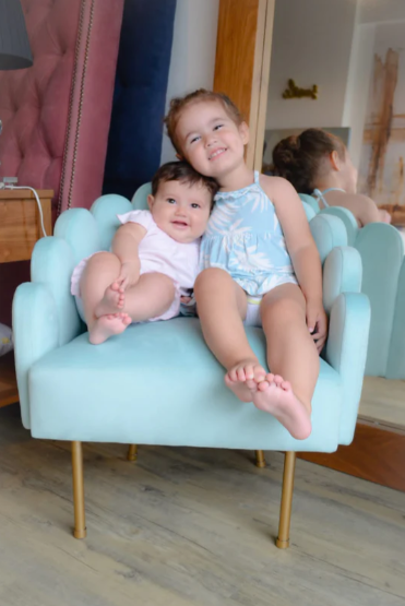 Sillón matero Mini Angie tapizado con respaldo y apoyabrazos de diseño ondulado y patas metálicas doradas.