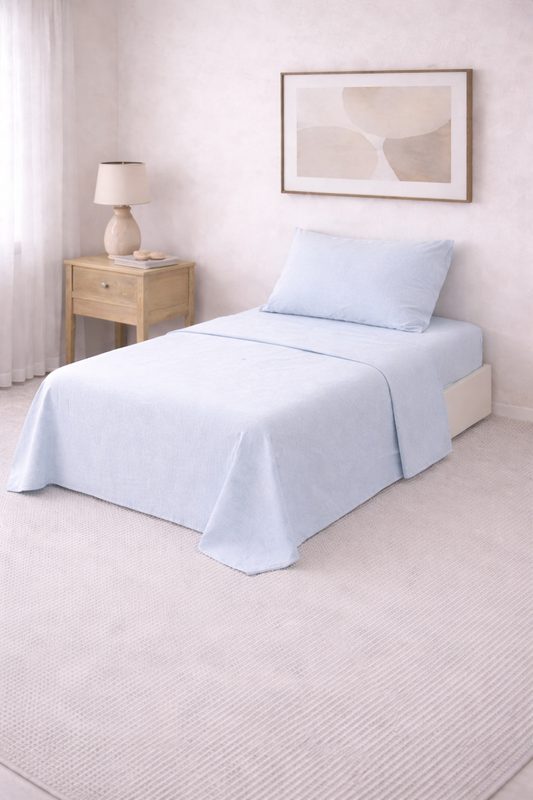 Cama de una plaza con sábanas lisas en tono suave, perfectamente tendida en un dormitorio luminoso de estilo minimalista con mesa de luz de madera y decoración neutra.