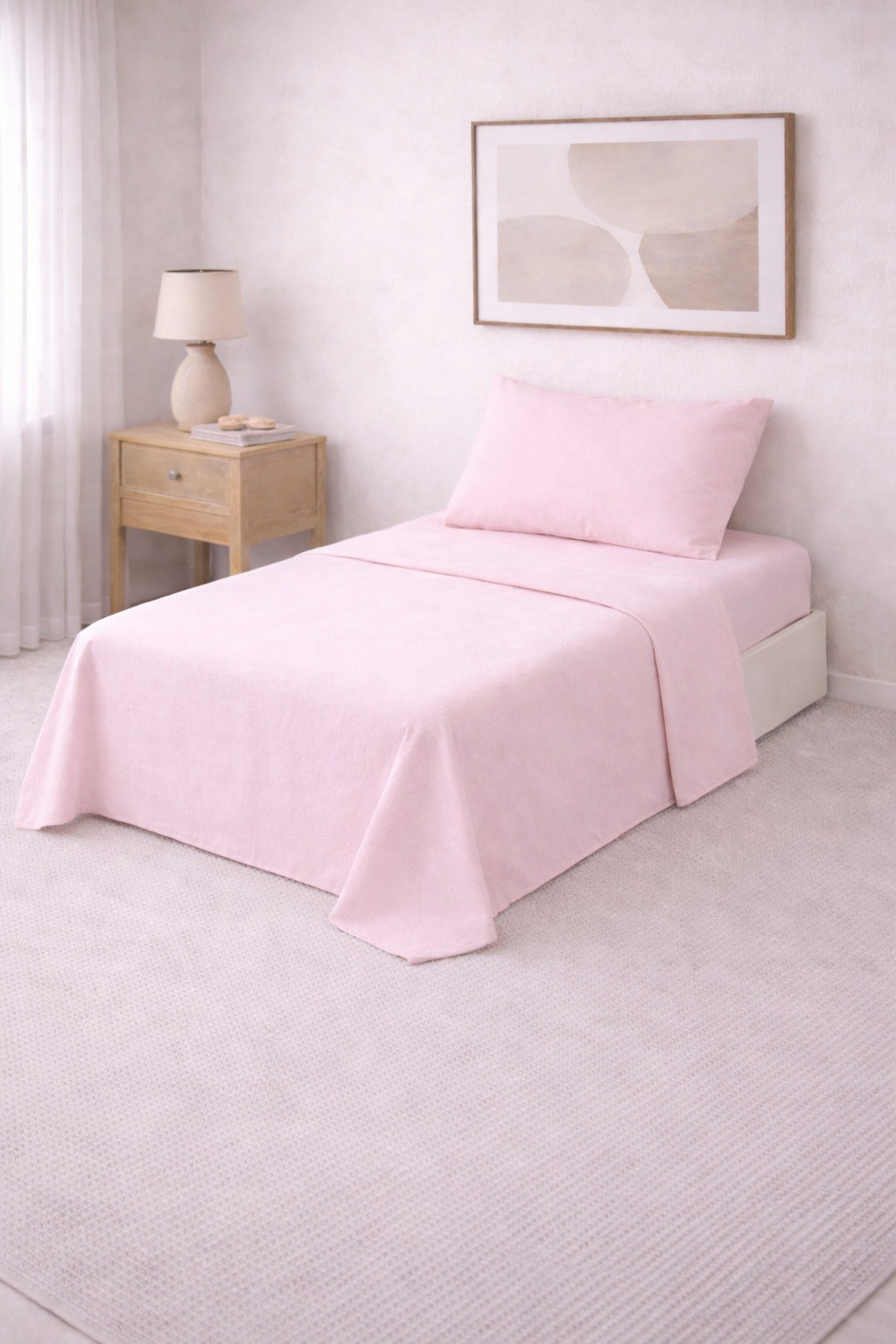 Cama de una plaza con sábanas lisas en tono suave, perfectamente tendida en un dormitorio luminoso de estilo minimalista con mesa de luz de madera y decoración neutra.