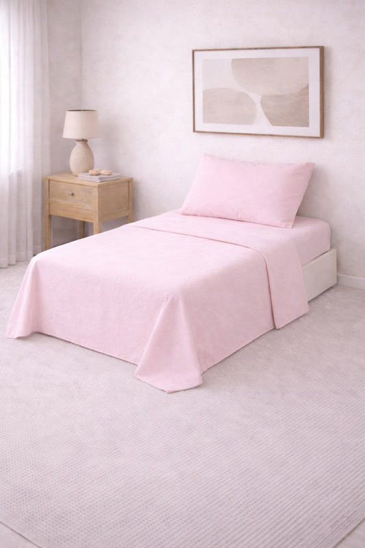 Cama de una plaza con sábanas lisas en tono suave, perfectamente tendida en un dormitorio luminoso de estilo minimalista con mesa de luz de madera y decoración neutra.