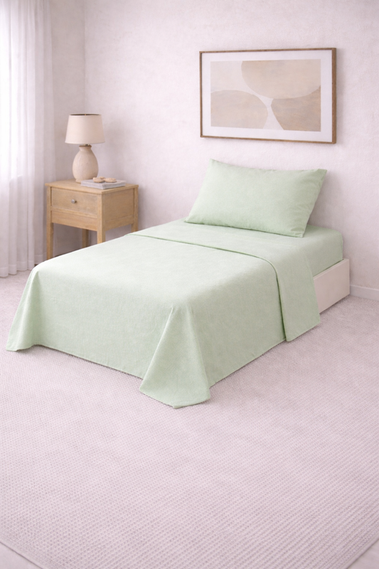 Cama de una plaza con sábanas lisas en tono suave, perfectamente tendida en un dormitorio luminoso de estilo minimalista con mesa de luz de madera y decoración neutra.