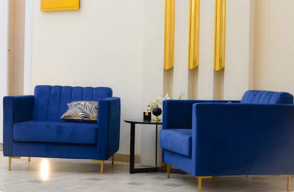 Sillón de un cuerpo Mila color Azul en pana antimanchas importada, ambientado junto a otro Mila en un living con detalles dorados — líneas rectas y patas de aluminio dorado opaco. Hecho a medida por Tienda de Banquitos.
