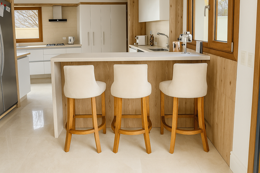 Cocina moderna con barra desayunadora de mármol, tres banquetas tapizadas en beige con patas de madera, muebles blancos y detalles en madera natural.