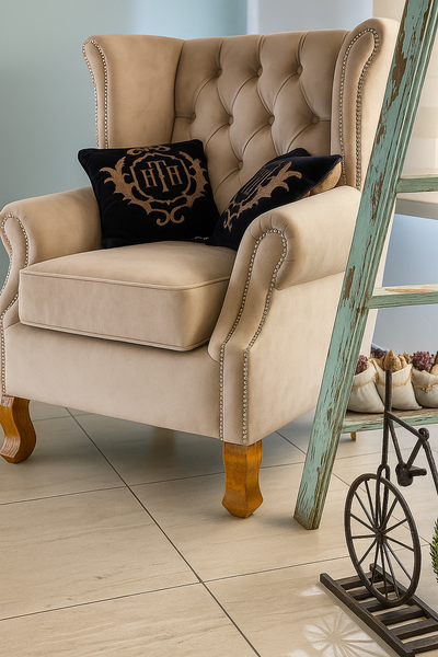 Sillón individual estilo clásico en tono beige, con tapizado capitoné y detalles de tachas metálicas en los brazos, acompañado por dos almohadones decorativos oscuros