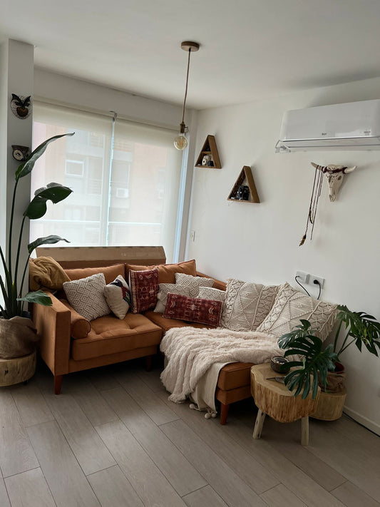 Un sillón esquinero tapizado en pana color terracota, decorado con almohadones tejidos en tonos neutros y una manta clara, que crean un ambiente cálido y natural en el living