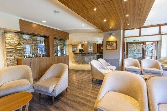 Salón del Hotel Carlos V en Bariloche ambientado con silloncitos París tapizados en tono neutro, dispuestos en forma circular con mesas de apoyo de madera.