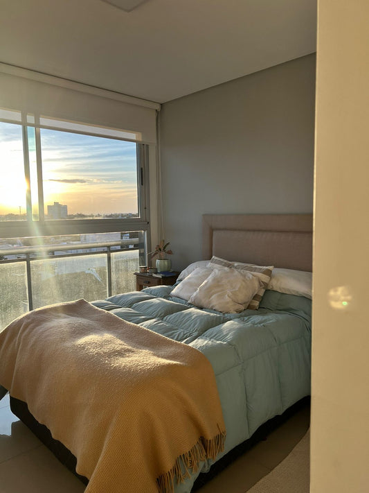 Respaldo de cama tapizado en tela color beige claro, de diseño recto y minimalista, acompañando una cama con acolchado celeste y almohadones decorativos en tonos neutros.