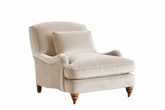 Sillón individual tapizado en beige claro, con cojín lumbar suelto, apoyabrazos curvos, respaldo levemente inclinado y patas torneadas de madera en tono medio.