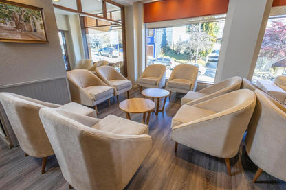 Salón del Hotel Carlos V en Bariloche ambientado con silloncitos París tapizados en tono neutro, dispuestos en forma circular con mesas de apoyo de madera.