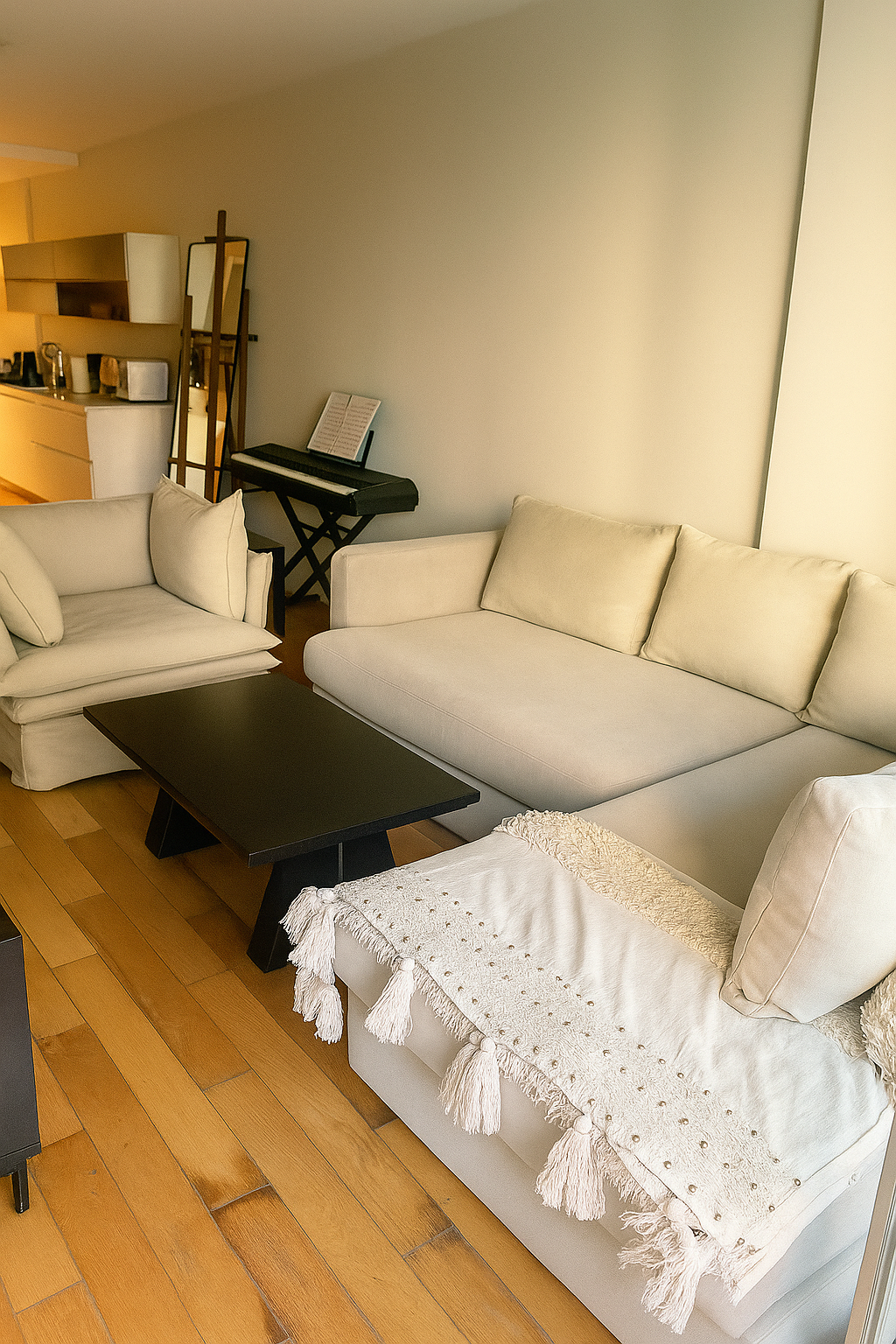 Living luminoso con mesa ratona rectangular negra, sofá esquinero beige y sillón de un cuerpo a juego, frente a un ventanal corredizo.