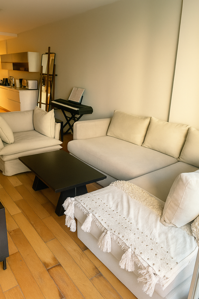 Living luminoso con mesa ratona rectangular negra, sofá esquinero beige y sillón de un cuerpo a juego, frente a un ventanal corredizo.
