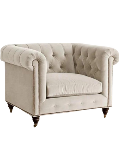 Sillón individual estilo Chesterfield tapizado en color gris claro, con capitoné en respaldo y apoyabrazos, tachas decorativas y patas de madera torneadas.