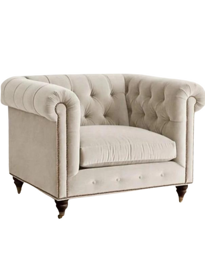 Sillón individual estilo Chesterfield tapizado en color gris claro, con capitoné en respaldo y apoyabrazos, tachas decorativas y patas de madera torneadas.